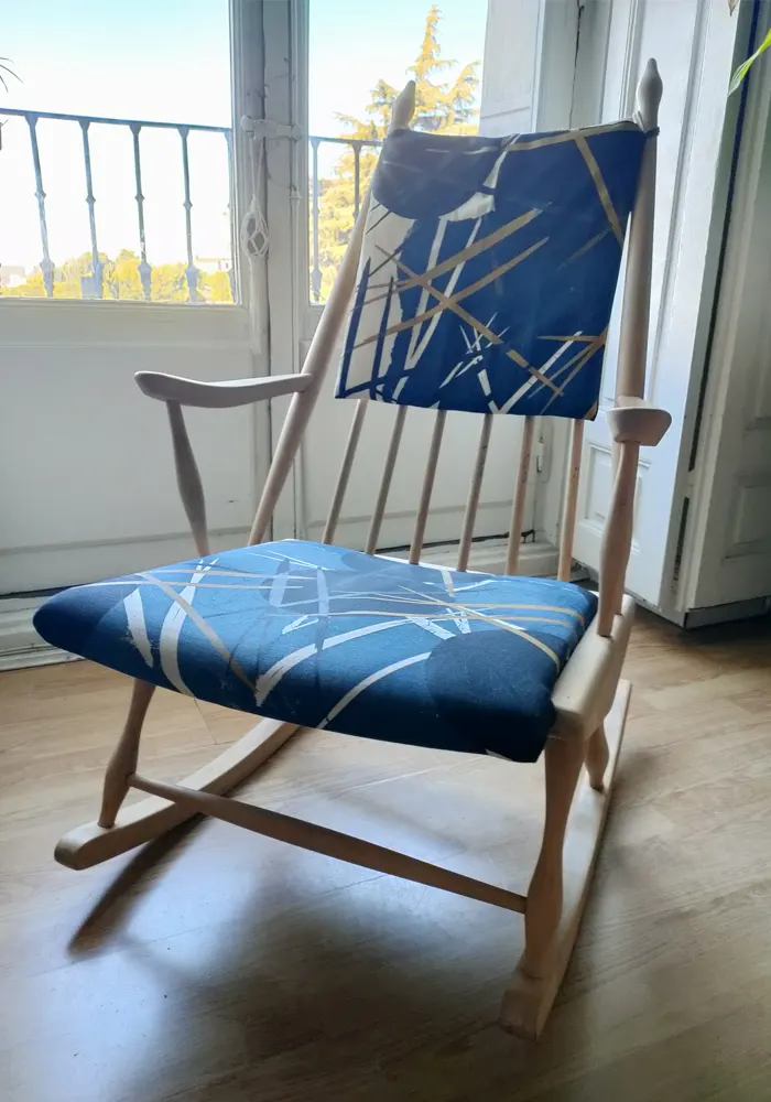 Mecedora de madera retapizada con tela estampada de color azul con dibujos de líneas en blanco y dorado