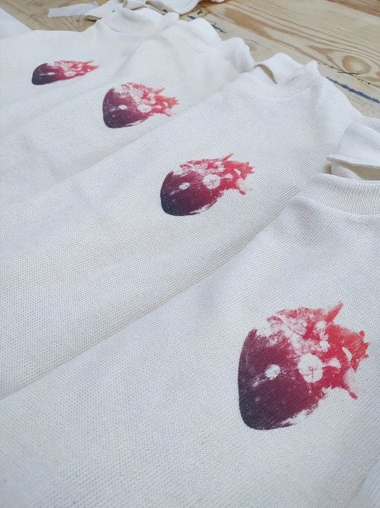Se muestra varias camisetas blancas con un estampado de colores rojizos de un corazón